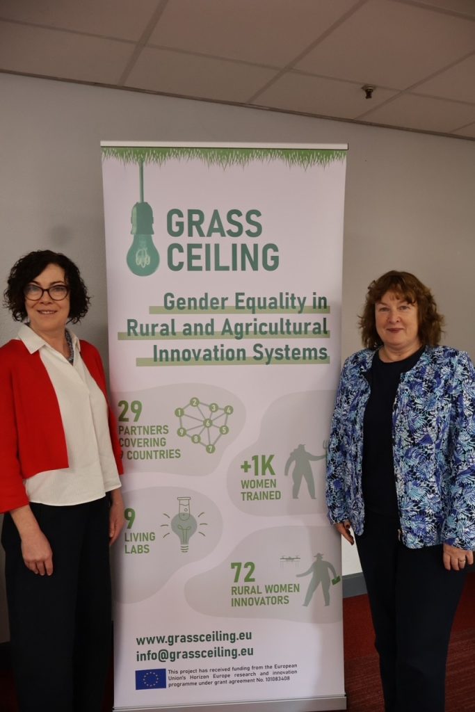 Project coordinator and academic standing next to Grass Ceiling Roll-up